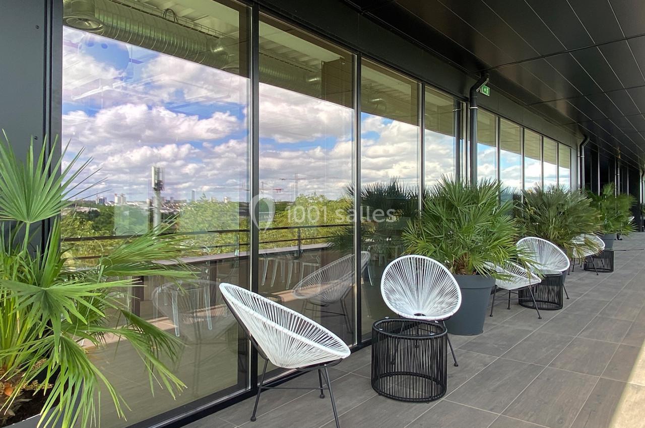 Terrasse moderne avec fauteuils design, tables basses et plantes, offrant une vue dégagée sur un paysage urbain.