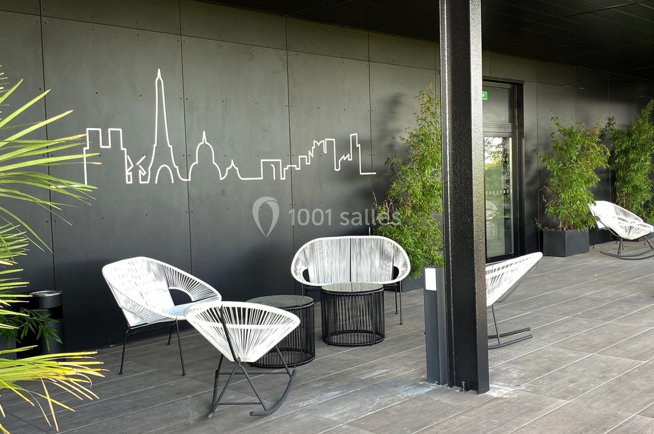 Terrasse moderne avec fauteuils en rotin, tables basses, plantes vertes et fresque murale représentant une skyline.
