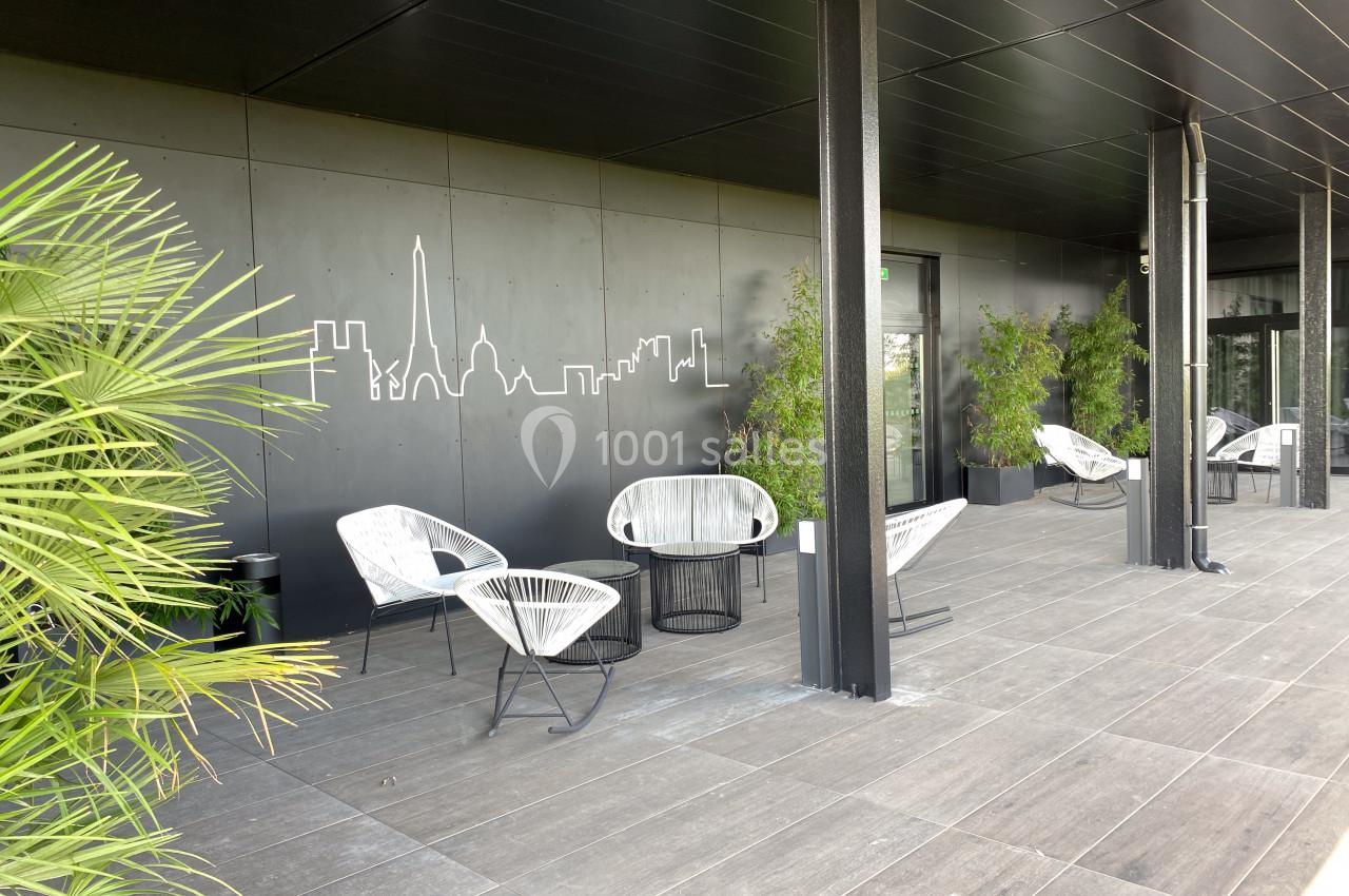 Terrasse moderne avec fauteuils design, plantes en pots et fresque murale représentant une silhouette urbaine.