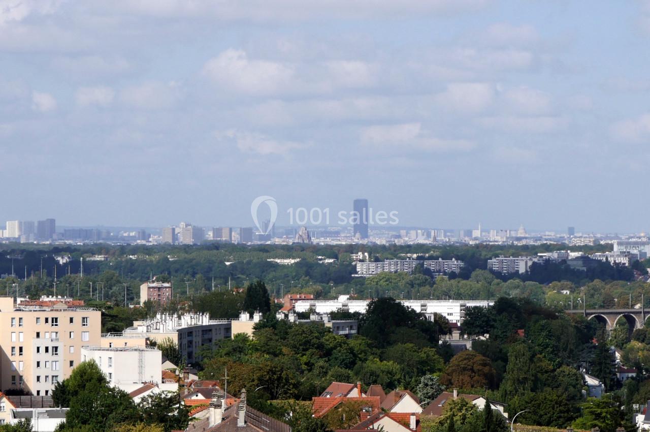 Vue panoramique d'une ville avec des immeubles, des espaces verts et un pont au premier plan sous un ciel partiellement…