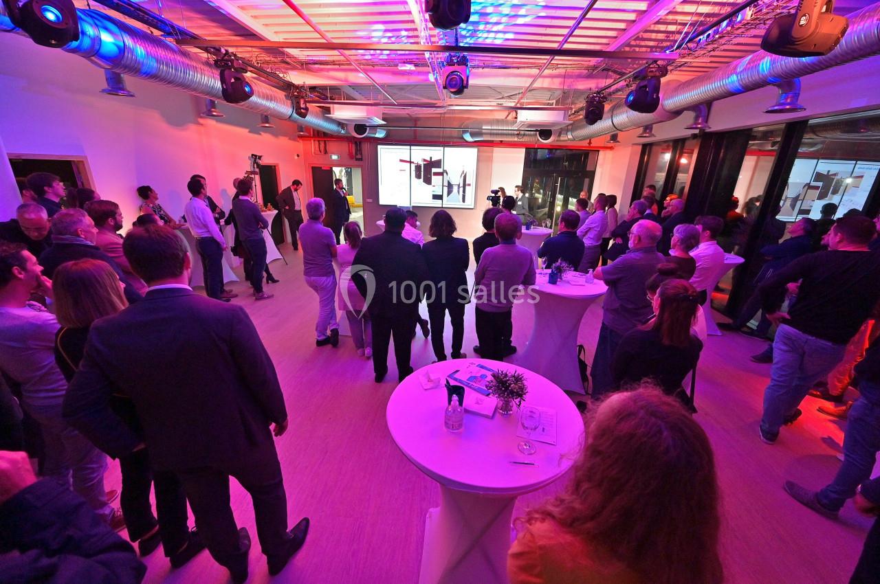 Groupe de personnes assistant à une présentation dans une salle éclairée par des lumières colorées.