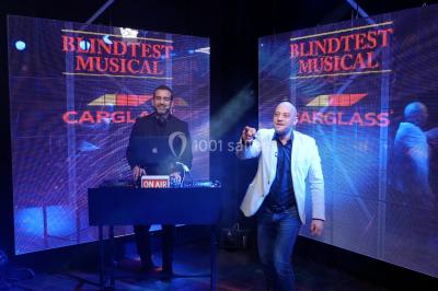 Miniature ArScénique #4 Homme sur une planche de surf simulant une vague géante gonflable dans un espace intérieur éclairé.