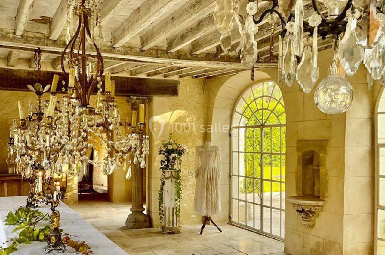 Salle lumineuse avec murs en pierre, lustres en cristal, table décorée et mannequin portant une robe légère.