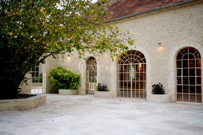 Portail en fer forgé ouvert sur un chemin verdoyant bordé d'arbres et de fleurs sauvages.