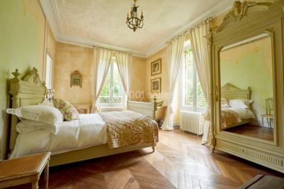 Portail en fer forgé ouvert sur un chemin verdoyant bordé d'arbres et de fleurs sauvages.