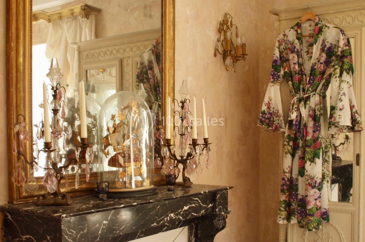 Manteau à motifs floraux suspendu près d'une armoire, avec un miroir doré et des chandeliers sur une cheminée en marbre.