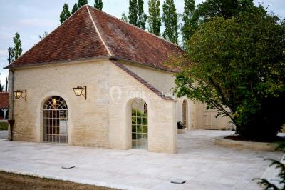 Portail en fer forgé ouvert sur un chemin verdoyant bordé d'arbres et de fleurs sauvages.