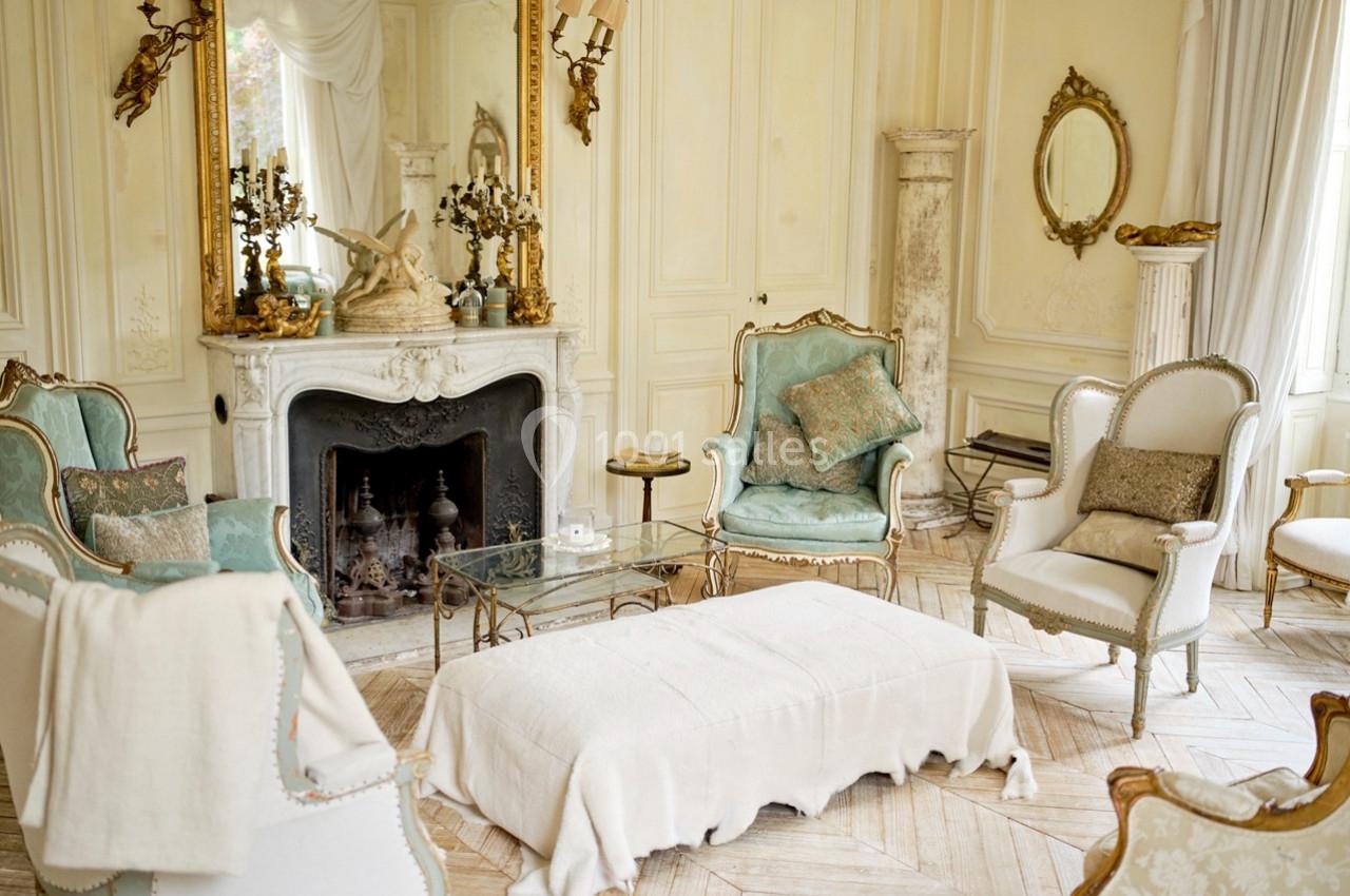 Salon élégant avec mobilier ancien, cheminée ornée, miroirs dorés et fauteuils rembourrés dans un décor lumineux.