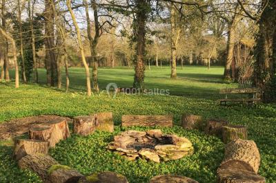 Portail en fer forgé ouvert sur un chemin verdoyant bordé d'arbres et de fleurs sauvages.