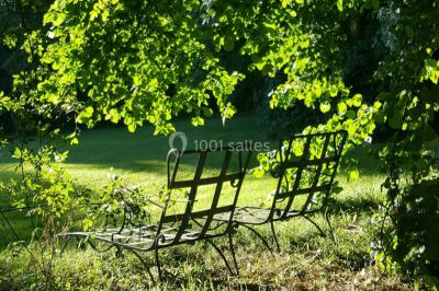 Portail en fer forgé ouvert sur un chemin verdoyant bordé d'arbres et de fleurs sauvages.