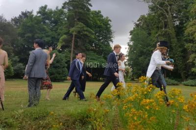 Portail en fer forgé ouvert sur un chemin verdoyant bordé d'arbres et de fleurs sauvages.