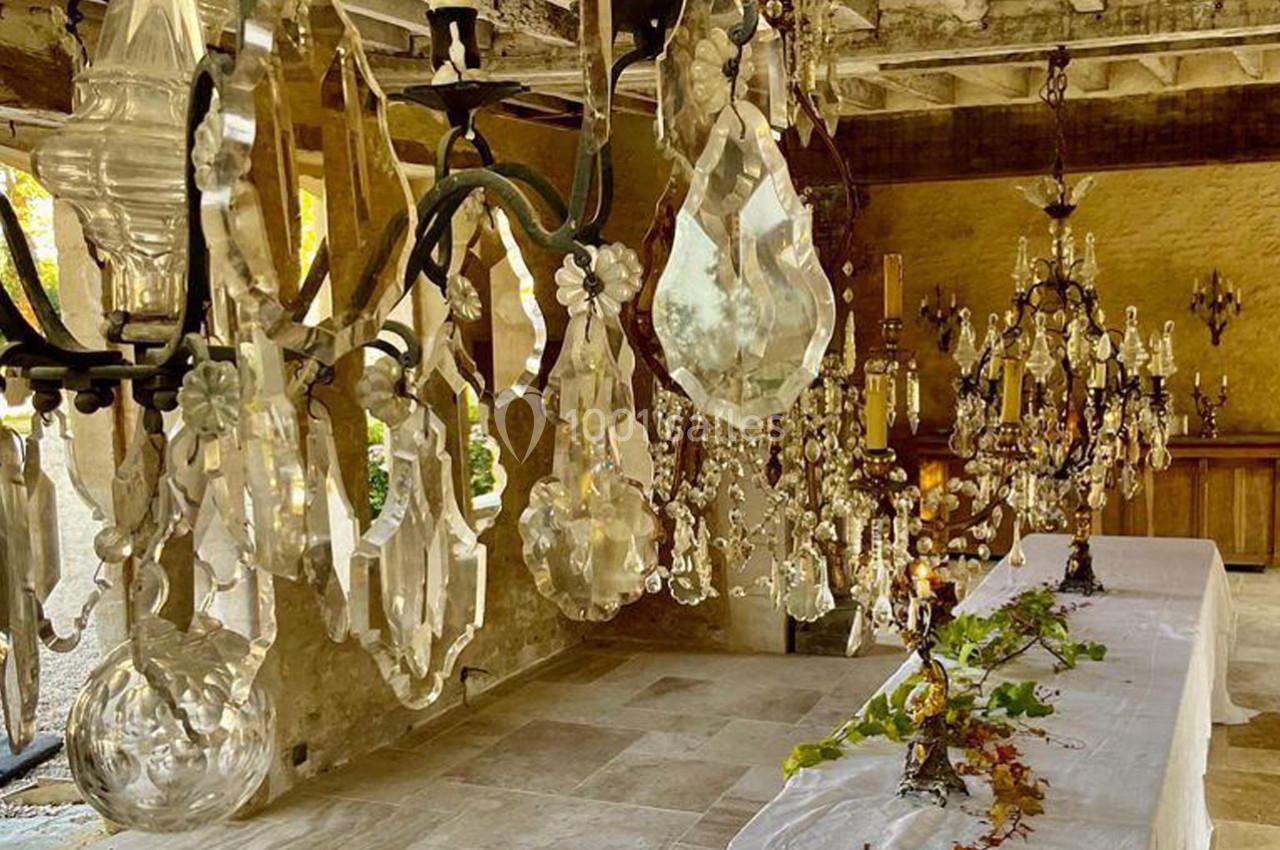 Des lustres en cristal suspendus dans une pièce rustique avec des tables décorées de feuillages.