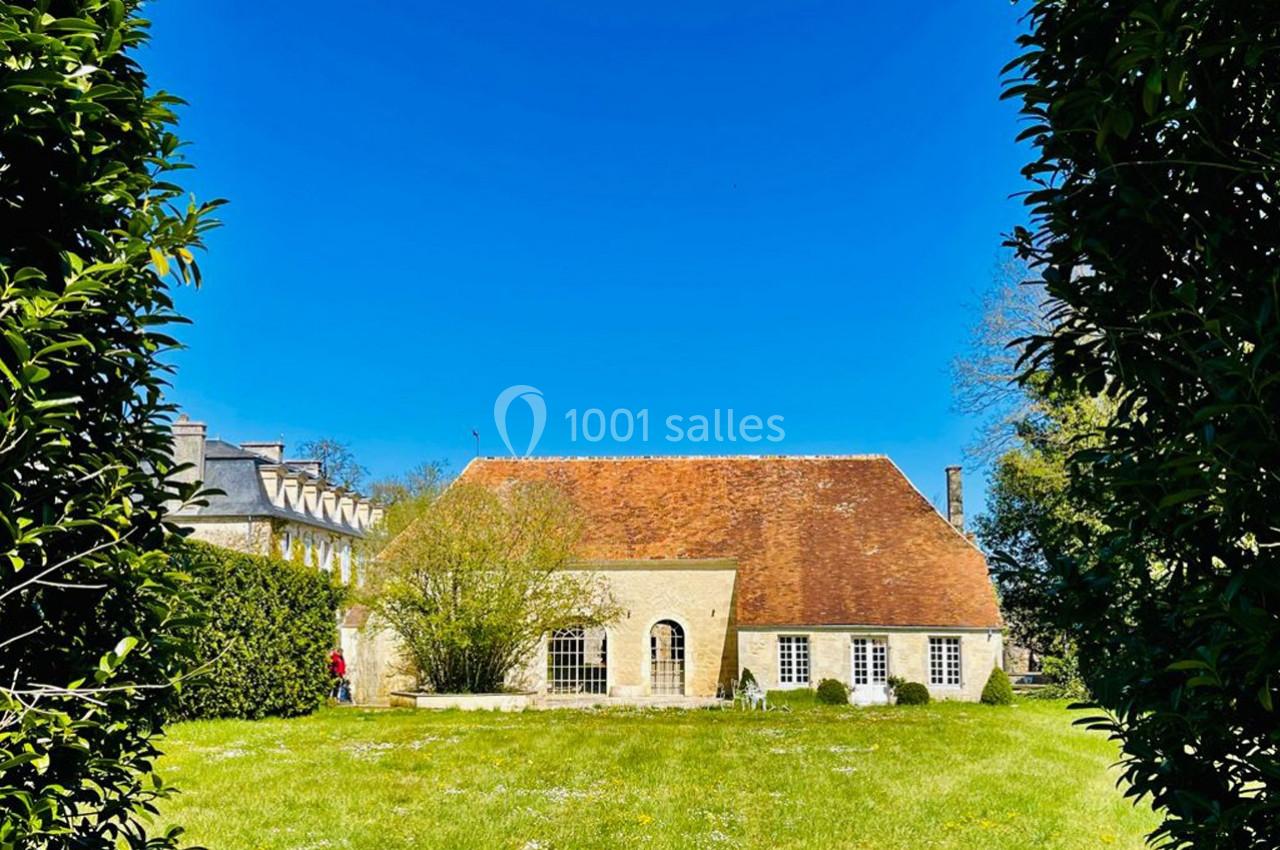Maison en pierre avec toit en tuiles rouges, entourée de verdure, sous un ciel bleu dégagé.