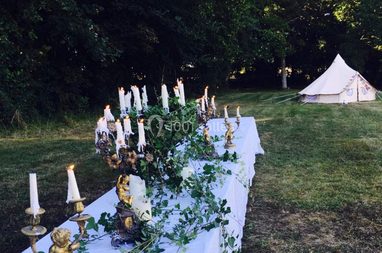Table décorée de chandeliers et de feuillage dans un jardin, avec une tente blanche en arrière-plan.
