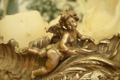 Statue en métal représentant un ange ailé allongé sur un décor ornemental aux détails sculptés.