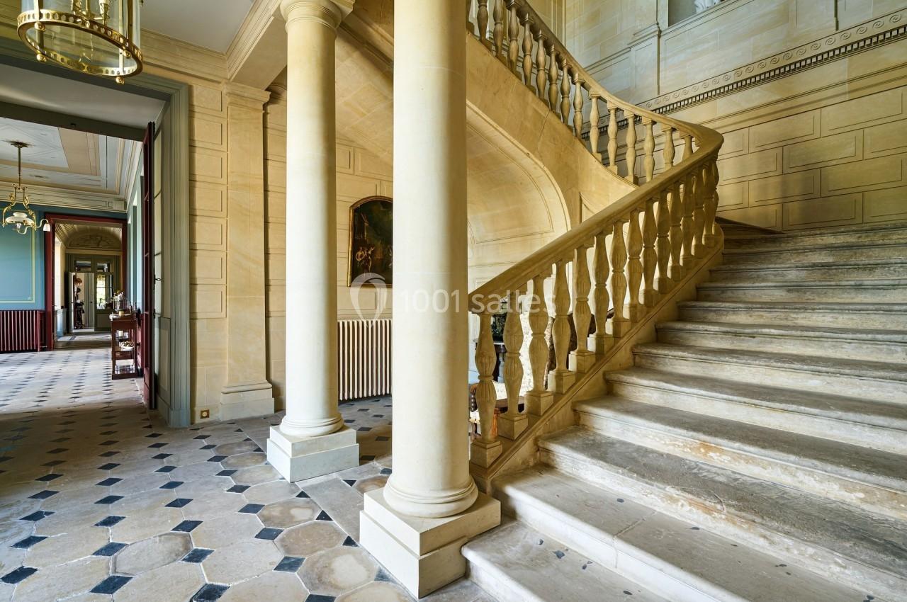 Escalier en pierre avec balustrade sculptée dans un intérieur lumineux aux murs clairs et sol en carreaux.