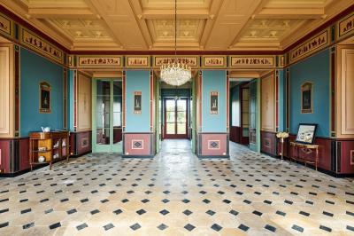 Salle élégante avec parquet en bois, murs ornés de moulures, lustres et mobilier classique.