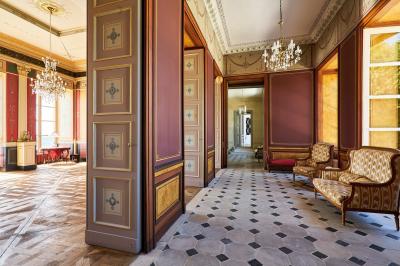 Salle élégante avec parquet en bois, murs ornés de moulures, lustres et mobilier classique.