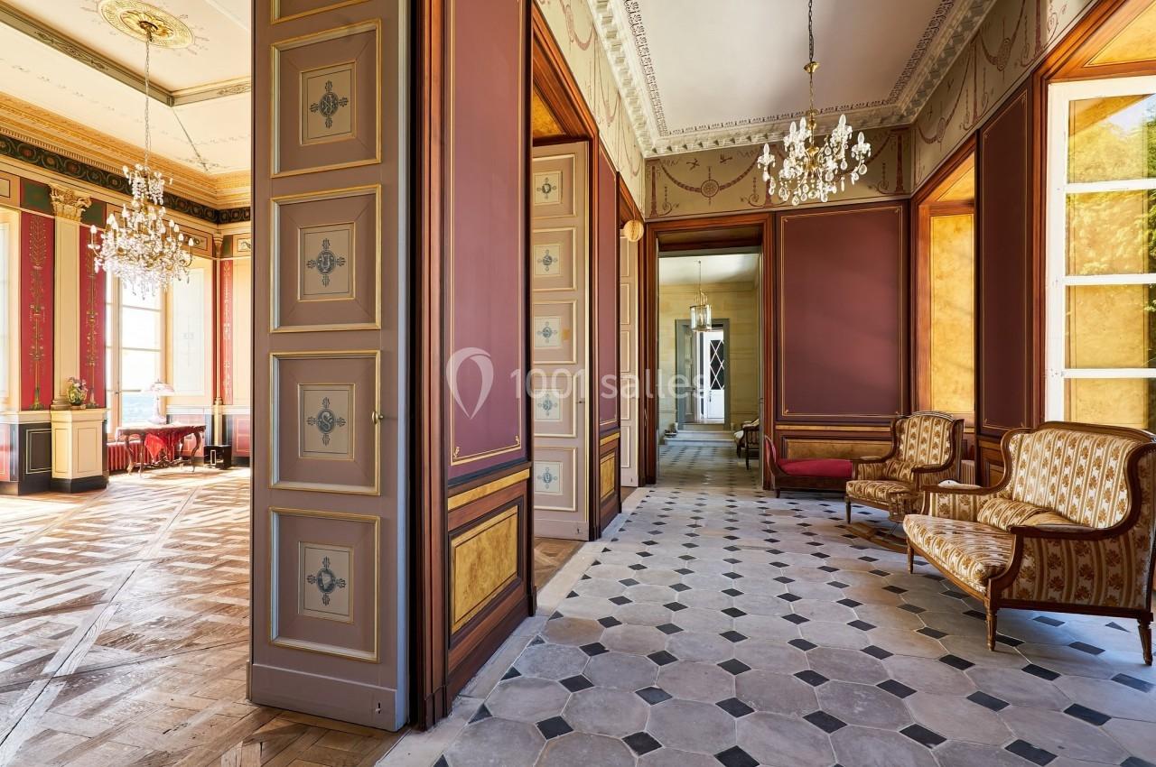 Intérieur d'un bâtiment ancien avec parquet, murs ornés, lustres et mobilier classique.