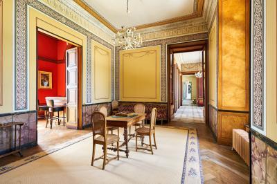 Salle élégante avec parquet en bois, murs ornés de moulures, lustres et mobilier classique.