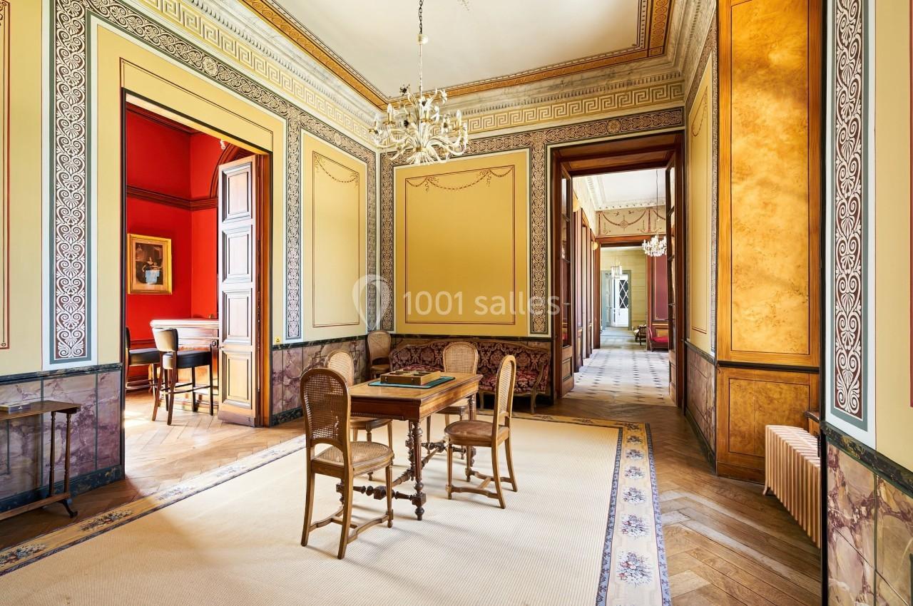 Salle élégante avec parquet en bois, murs ornés de moulures, lustres et mobilier classique.