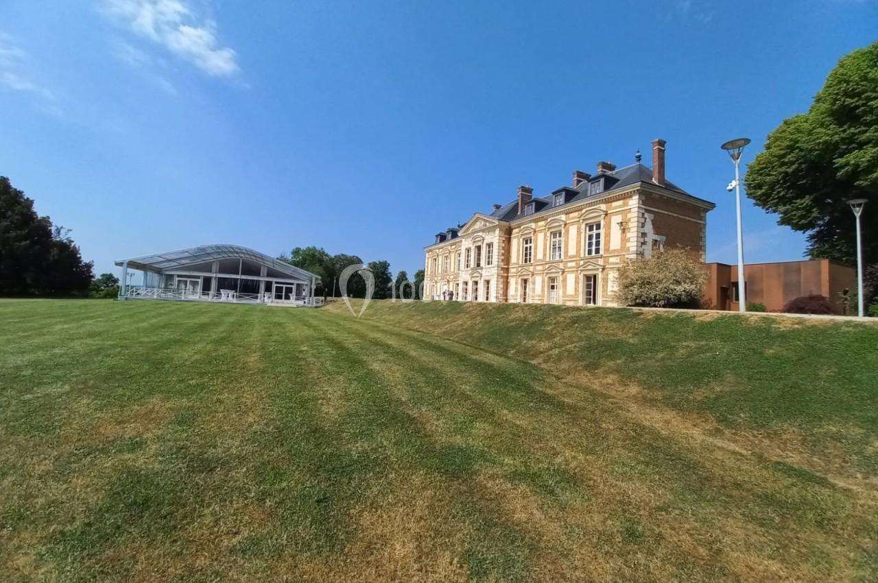 Vue d'un bâtiment historique en pierre avec un parc verdoyant et une structure moderne en arrière-plan.
