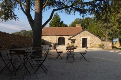 Terrasse extérieure avec pergola en bois, tables et chaises sur sol gravillonné, près d'un mur en pierre et d'un arbre.