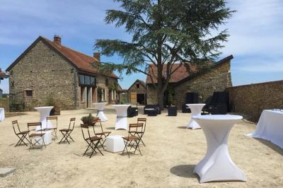 Terrasse extérieure avec pergola en bois, tables et chaises sur sol gravillonné, près d'un mur en pierre et d'un arbre.