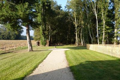 Terrasse extérieure avec pergola en bois, tables et chaises sur sol gravillonné, près d'un mur en pierre et d'un arbre.