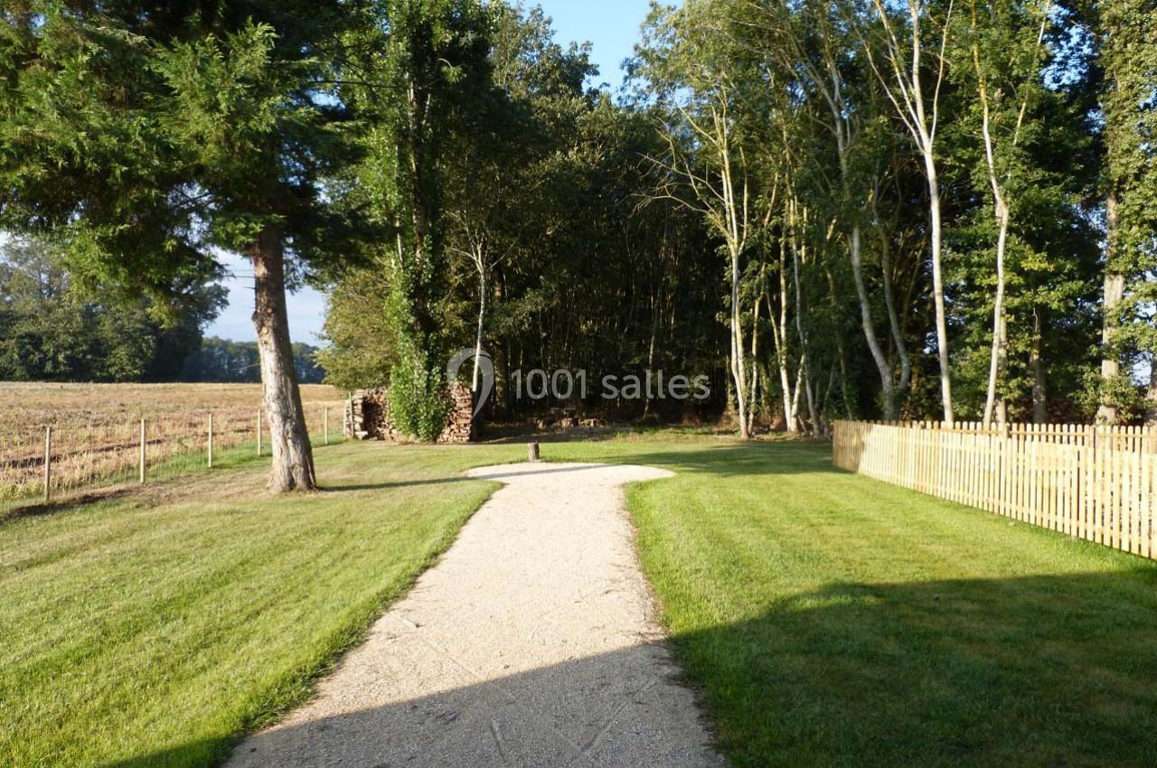 Chemin de gravier bordé de pelouses, menant à une zone boisée sous un ciel dégagé.