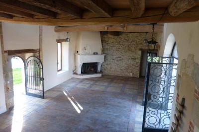 Terrasse extérieure avec pergola en bois, tables et chaises sur sol gravillonné, près d'un mur en pierre et d'un arbre.