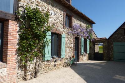 Terrasse extérieure avec pergola en bois, tables et chaises sur sol gravillonné, près d'un mur en pierre et d'un arbre.