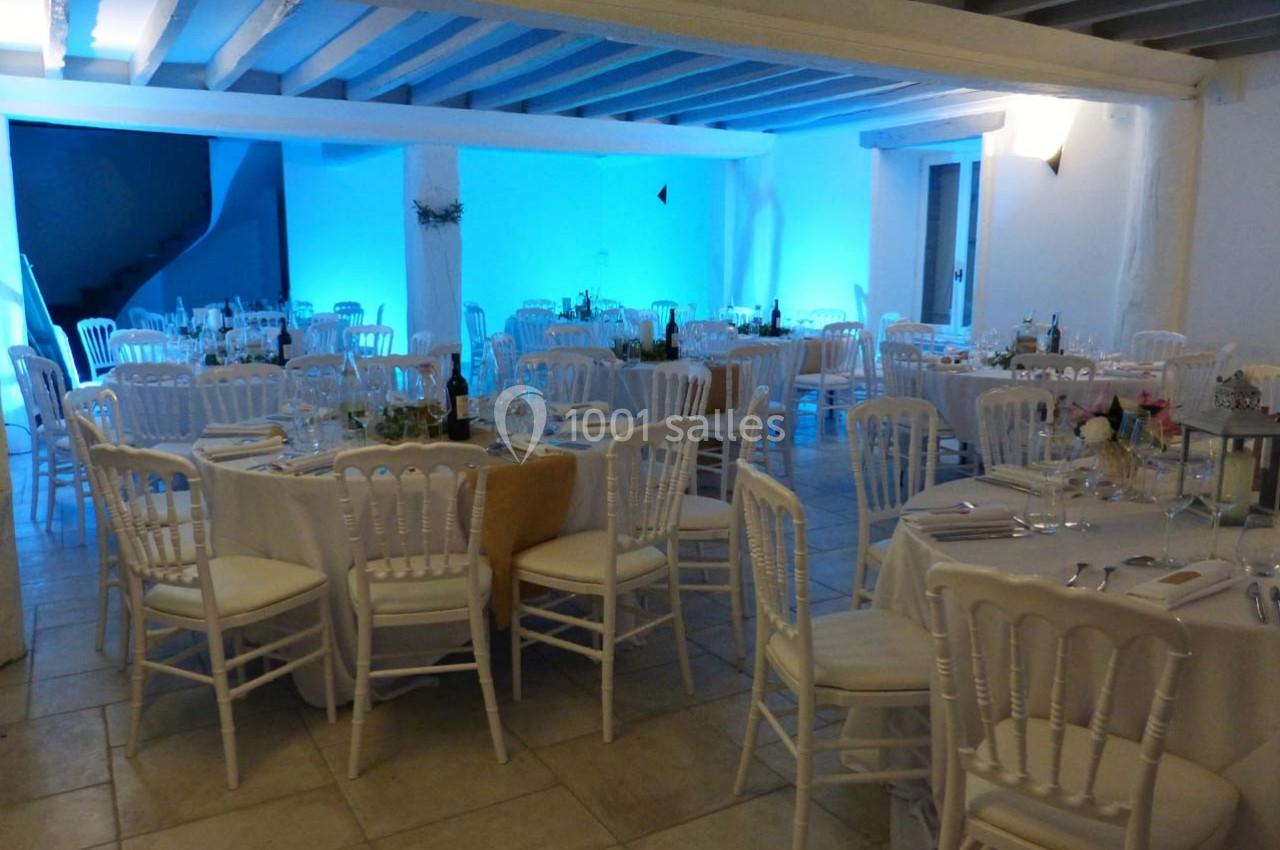 Salle de réception décorée avec des tables rondes dressées, chaises blanches et éclairage bleu tamisé.