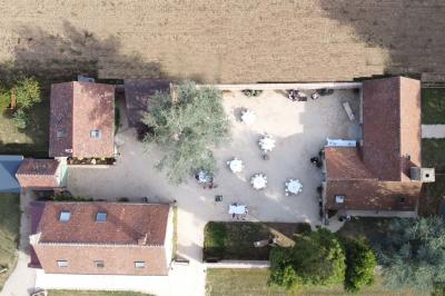 Terrasse extérieure avec pergola en bois, tables et chaises sur sol gravillonné, près d'un mur en pierre et d'un arbre.