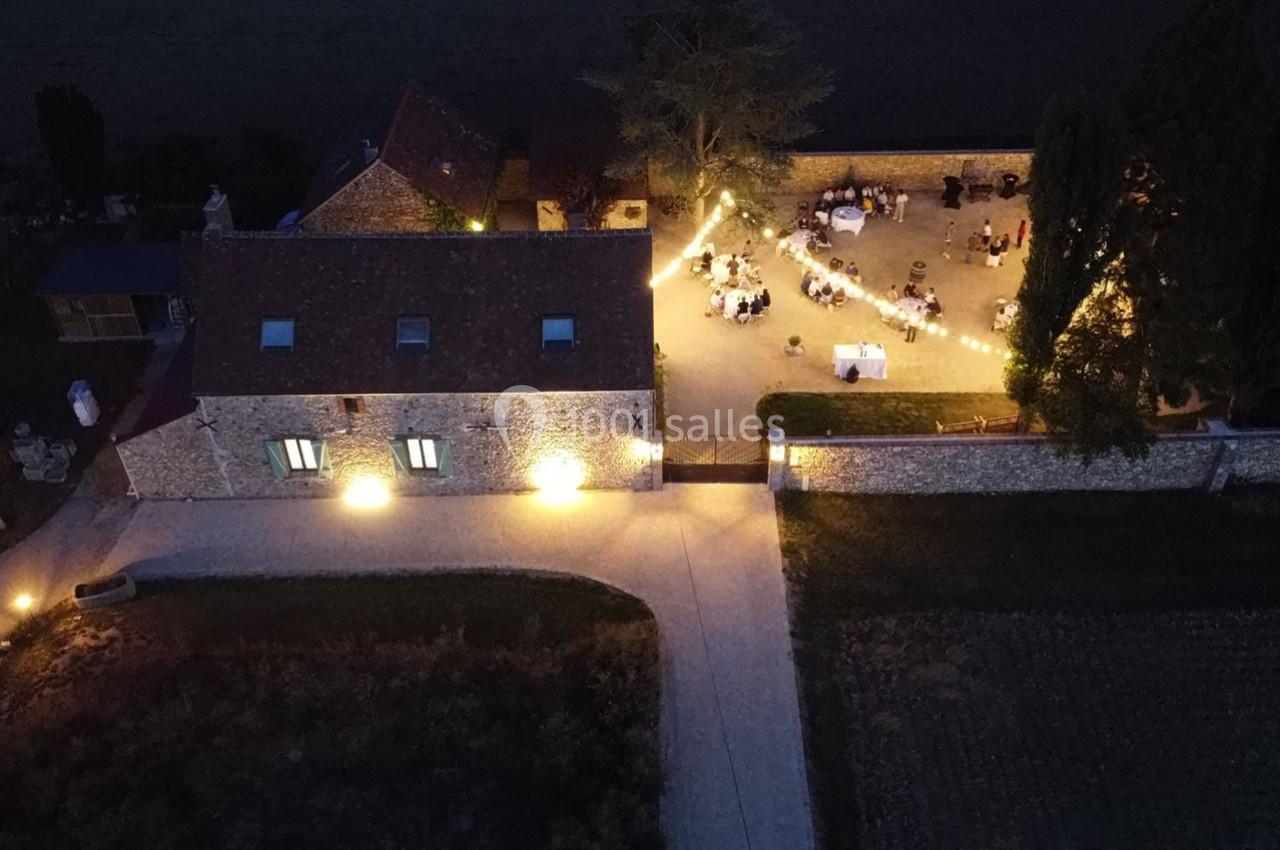 Vue aérienne nocturne d'une cour éclairée par des guirlandes lumineuses, entourée de bâtiments en pierre.