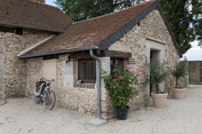 Terrasse extérieure avec pergola en bois, tables et chaises sur sol gravillonné, près d'un mur en pierre et d'un arbre.