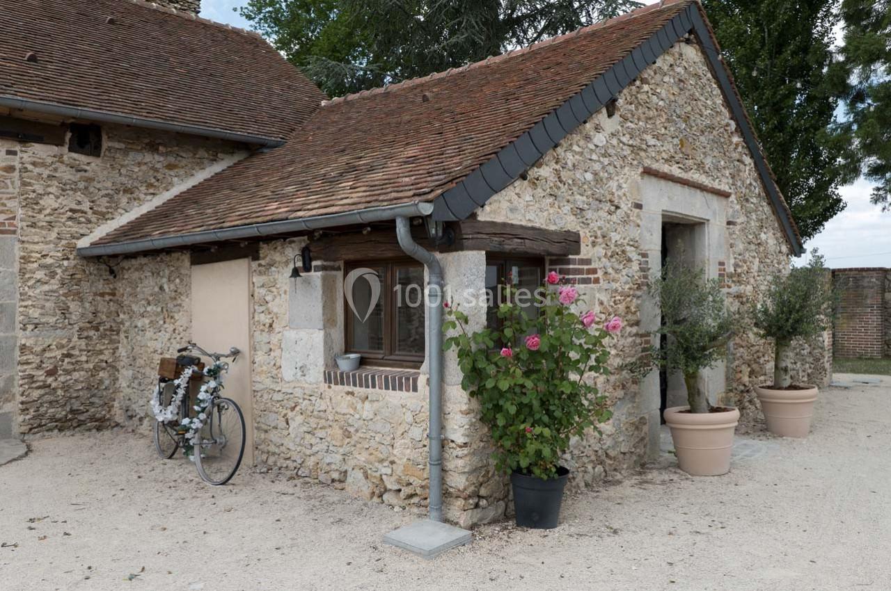 Façade en pierre d'une maison traditionnelle avec toit en tuiles, vélo appuyé contre le mur et plantes en pot.
