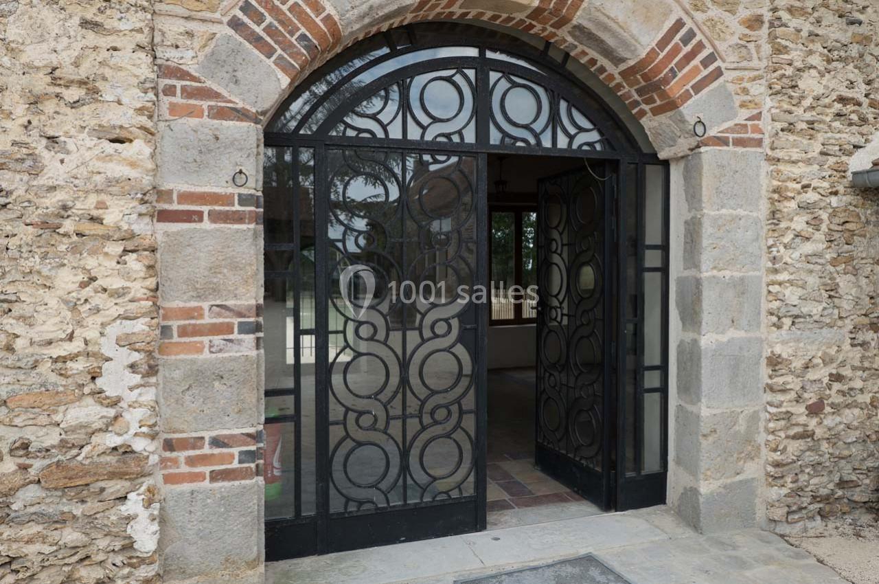 Porte en fer forgé avec motifs circulaires, encadrée par une arche en pierre et briques, donnant sur un intérieur lumineux.