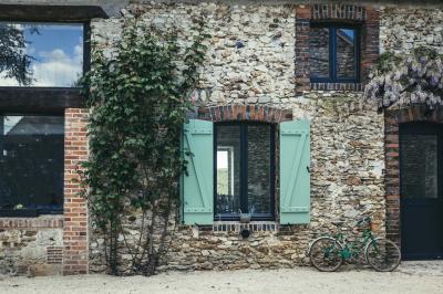 Terrasse extérieure avec pergola en bois, tables et chaises sur sol gravillonné, près d'un mur en pierre et d'un arbre.