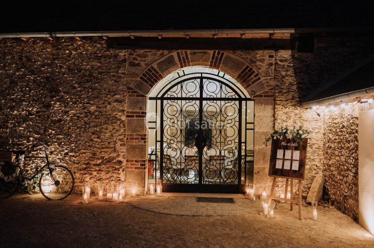 Entrée d'un bâtiment en pierre avec une porte en fer forgé, entourée de bougies et d'une décoration lumineuse.