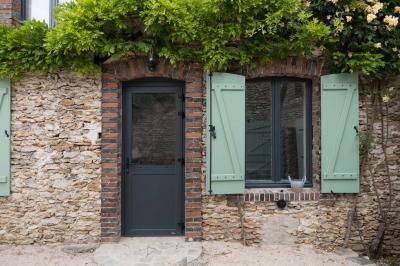 Terrasse extérieure avec pergola en bois, tables et chaises sur sol gravillonné, près d'un mur en pierre et d'un arbre.