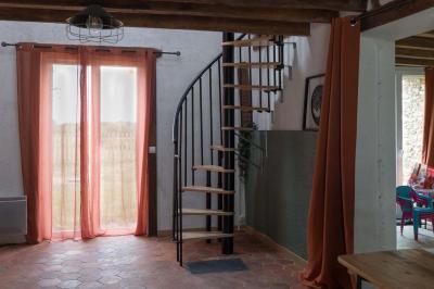 Terrasse extérieure avec pergola en bois, tables et chaises sur sol gravillonné, près d'un mur en pierre et d'un arbre.