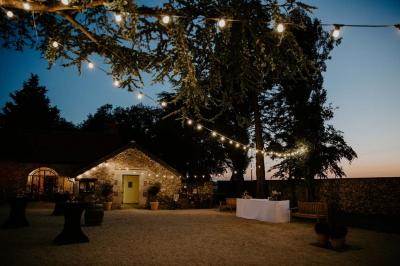 Terrasse extérieure avec pergola en bois, tables et chaises sur sol gravillonné, près d'un mur en pierre et d'un arbre.