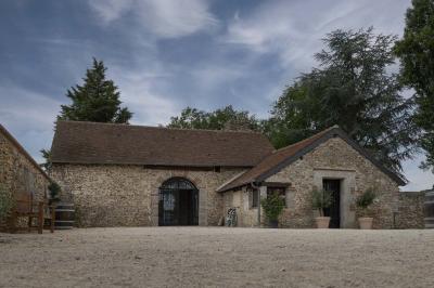Terrasse extérieure avec pergola en bois, tables et chaises sur sol gravillonné, près d'un mur en pierre et d'un arbre.