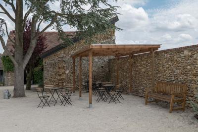Terrasse extérieure avec pergola en bois, tables et chaises sur sol gravillonné, près d'un mur en pierre et d'un arbre.