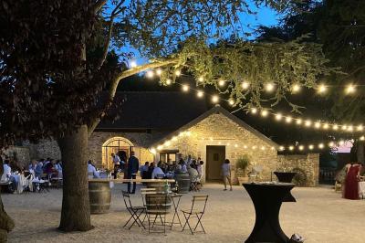 Terrasse extérieure avec pergola en bois, tables et chaises sur sol gravillonné, près d'un mur en pierre et d'un arbre.