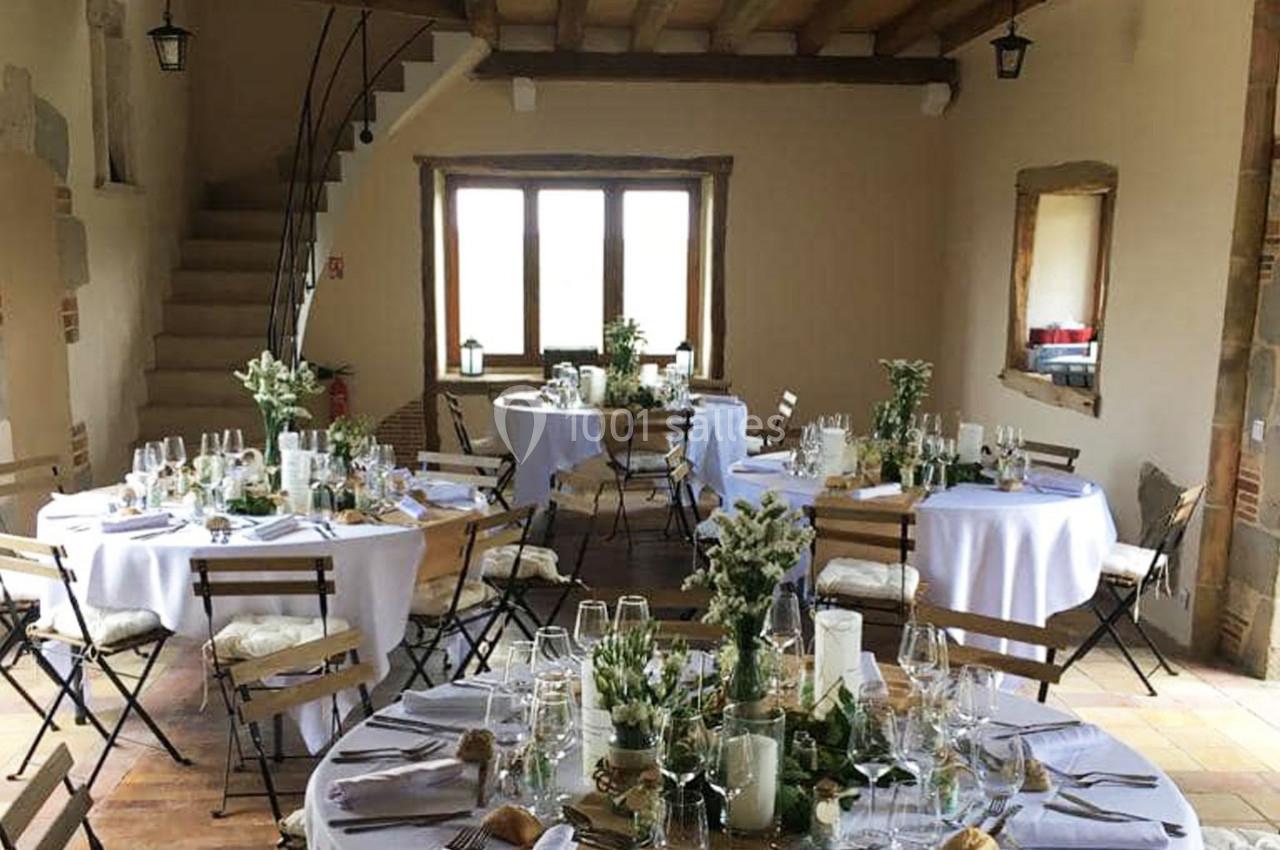 Salle décorée pour un événement avec tables rondes dressées, nappes blanches et arrangements floraux.