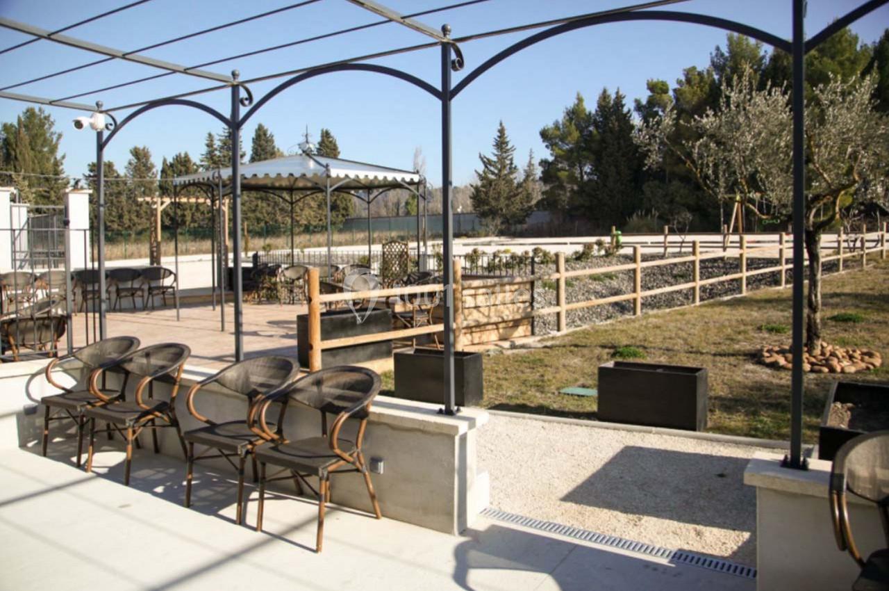 Terrasse extérieure avec chaises, pergola et vue sur un jardin arboré entouré de clôtures en bois.