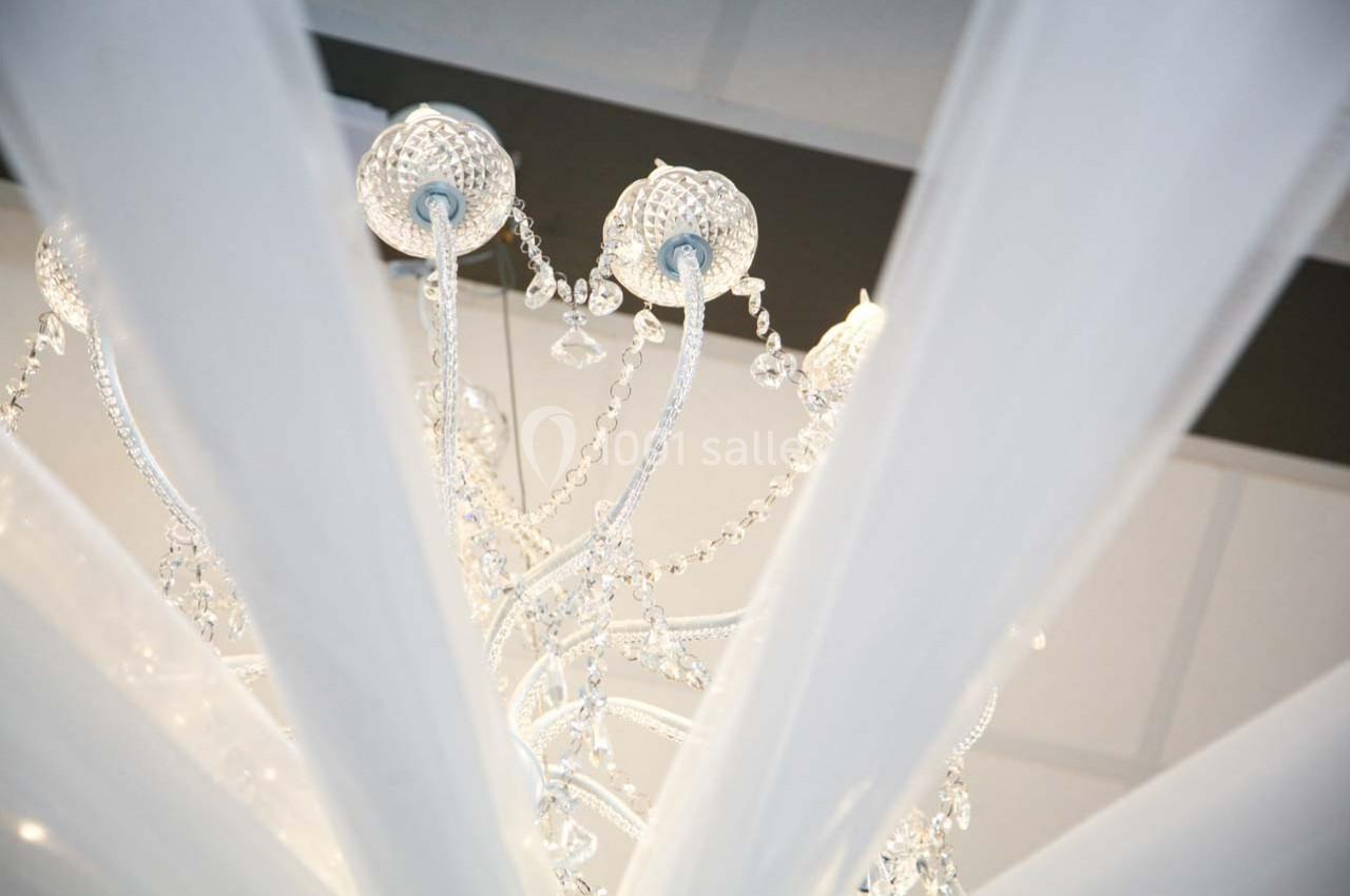 Lustre en cristal vu de dessous, entouré de voiles blancs suspendus, dans un intérieur lumineux.