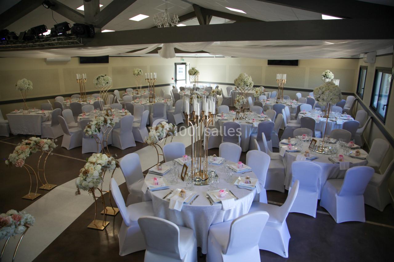 Salle de réception décorée pour un mariage avec des tables rondes, nappes blanches, chandeliers et arrangements floraux.